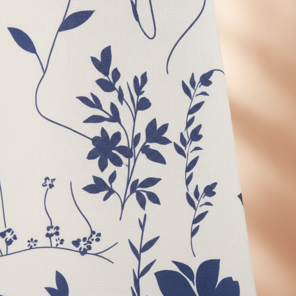 Close-up of AURELIA garment fabric, showing a detailed mid-century botanical print in warm cream and soft peach tones.
